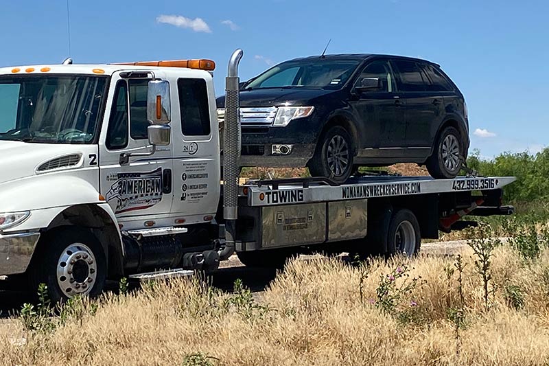 Flatbed tow truck loaded with an SUV on a country road Team America Towing Odessa Tow Service